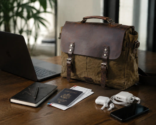 Leather messenger briefcase on a wooden desk with laptop, passport, notebook, and travel essentials in a warm, realistic business workspace setting