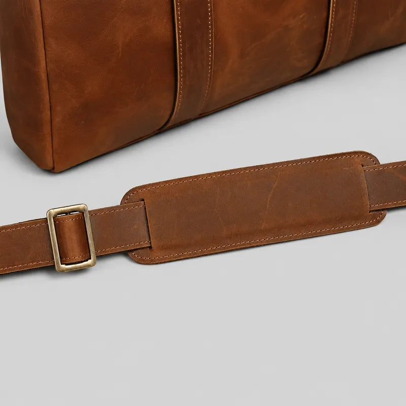 Close-up of leather shoulder strap with padded section and brass buckle on brown crazy horse leather briefcase