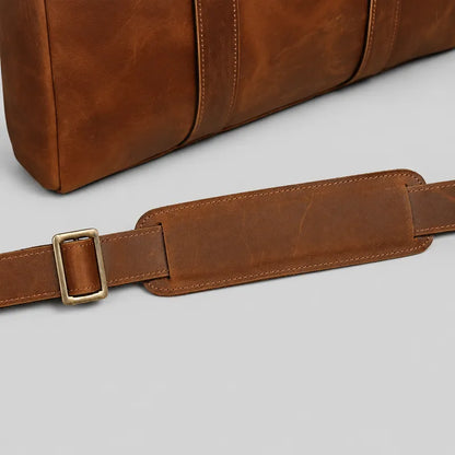 Close-up of leather shoulder strap with padded section and brass buckle on brown crazy horse leather briefcase