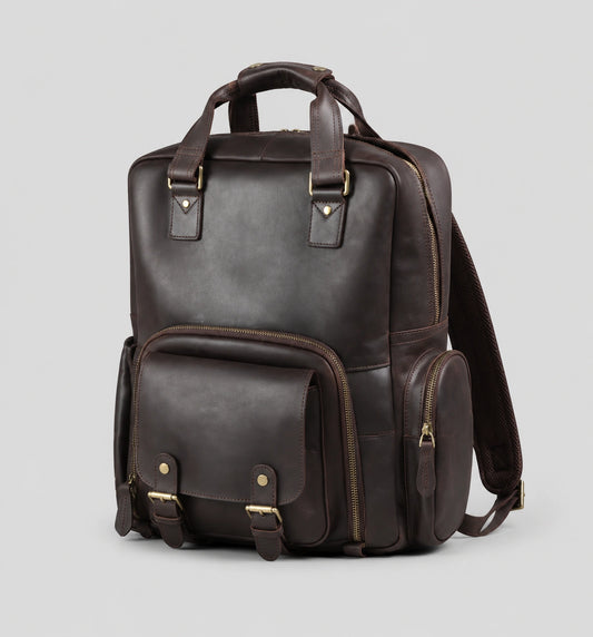 Dark brown Crazy Horse leather camera backpack on a light gray background, showing front view with top handle, front flap pocket with buckles, side pocket, and durable brass hardware. Suitable for DSLR cameras, laptop, and travel essentials.