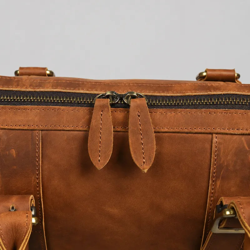 Close-up of brass zipper hardware and leather pull tabs on brown crazy horse leather briefcase